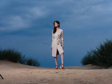 Sundress giymiş bir kadının uzun bir portresi ve kumsalda kırmızı sandaletler.