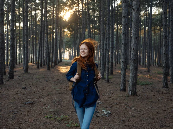 Mujer Turista con una mochila en un bosque de pinos y puesta de sol en el fondo —  Fotos de Stock