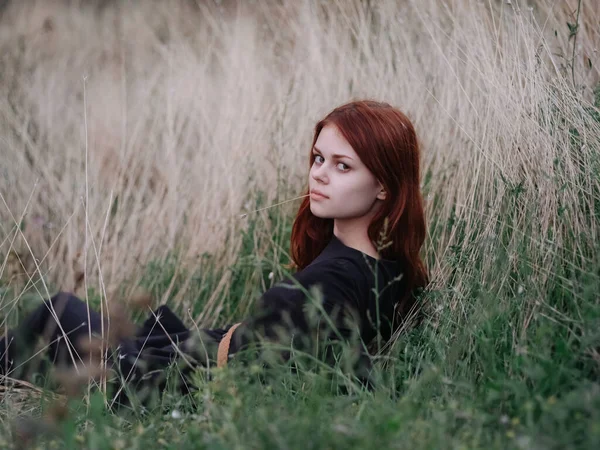 Femme aux cheveux roux dans une robe noire repose sur l'herbe sèche dans la nature — Photo