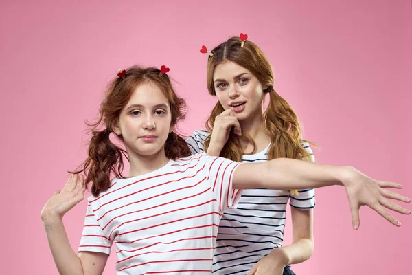 Hermanas felices se divierten en un fondo rosa y pinzas de ropa en forma de corazón en sus cabezas — Foto de Stock