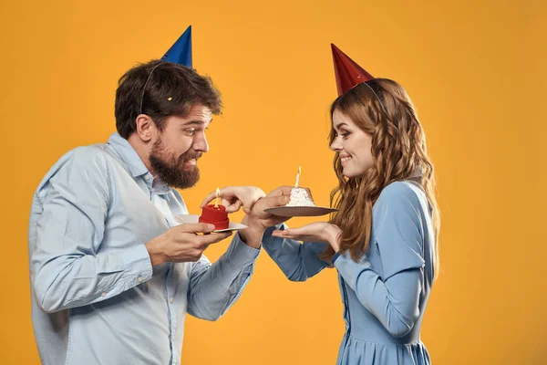 誕生日パーティー男と女でキャップでAケーキとともに黄色の背景トリミングされたビュー — ストック写真