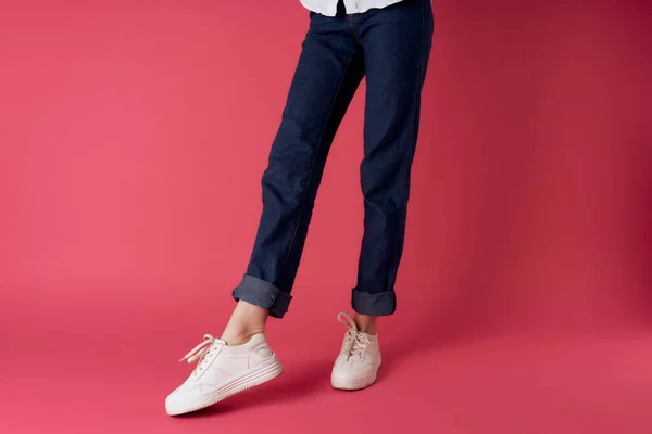 Donna gambe jeans bianco sneakers strada moda studio rosa sfondo — Foto Stock