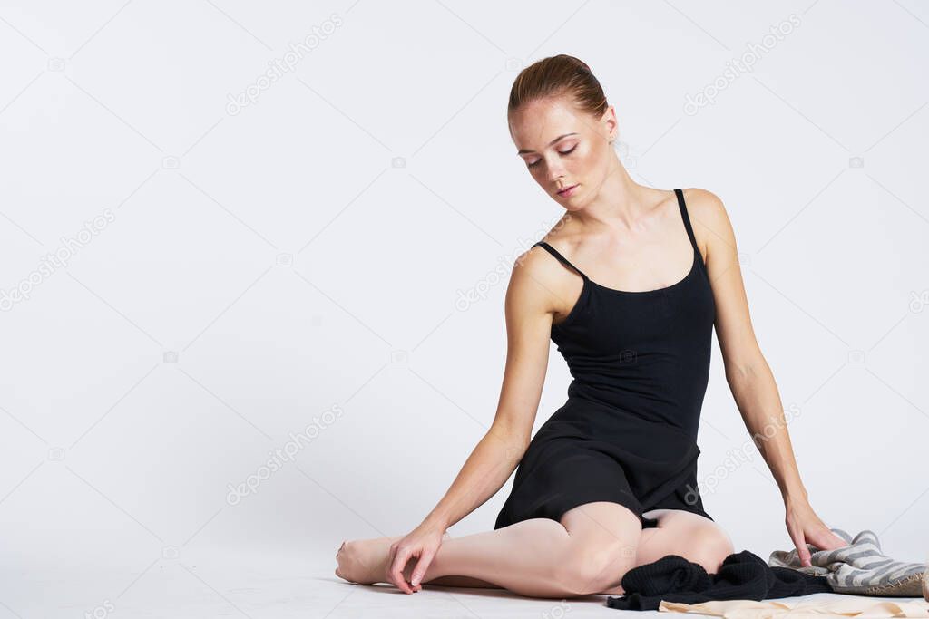 A ballerina in a black dress on a light background performs dance exercises striped socks planty tutu model