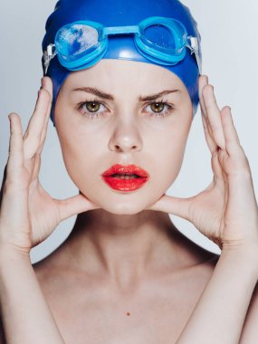 Mavi yüzme şapkalı güzel kadın elleriyle ve gözlükleriyle yüzüne dokunuyor.