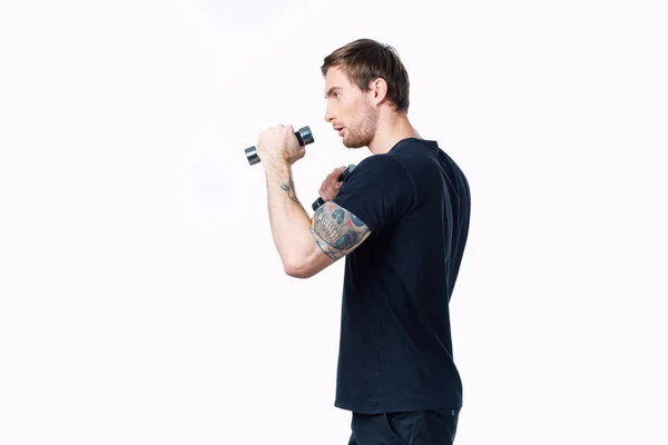 Forte atleta uomo in una t-shirt nera facendo esercizi con manubri nelle sue mani fitness — Foto Stock