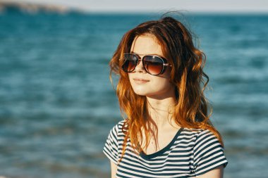 Deniz kenarındaki dağlarda güneş gözlüklü kızıl saçlı bir kadının portresi ve kahkahalar atan bir seyahat. 