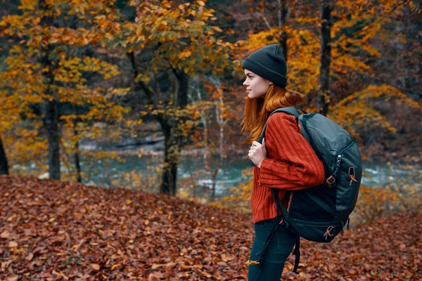 Foglie cadute nel parco in autunno e il fiume sullo sfondo donna turista con uno zaino di viaggio — Foto Stock