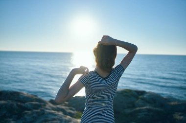 Mutlu bir seyyah kadın, elleri denizin kenarında, doğada ve gün batımında uzakta el kol geziyor.