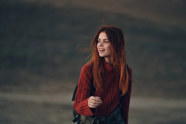 Bella donna in un maglione con uno zaino stanno camminando nella natura in montagna su un prato — Foto Stock