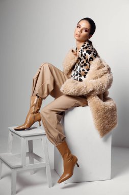 Yüzünde parlak makyajlı kadın kahverengi çizmeli moda leopar gömlekli.