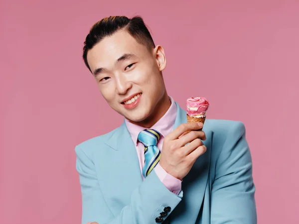 Egy vidám férfi klasszikus öltönyös gesztusokkal, rózsaszín háttérrel és fagylaltmodellel. — Stock Fotó