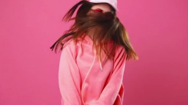 Güzel gülüşü olan mutlu bir kadın dans ediyor ve pembe bir arka planda zıplıyor, olumlu duygular içinde.