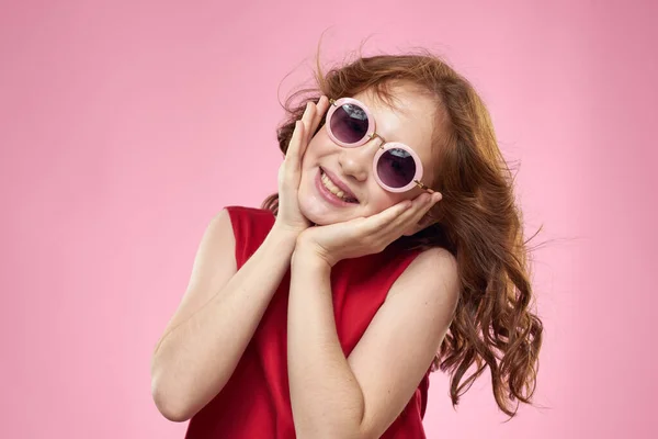 Menina alegre infância óculos escuros vestido vermelho estilo de vida fundo rosa — Fotografia de Stock