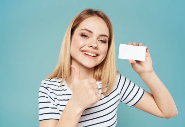 Mavi arka planda mutlu bir kadın elleri ve elinde bir kartvizitle el kol hareketi yapar.