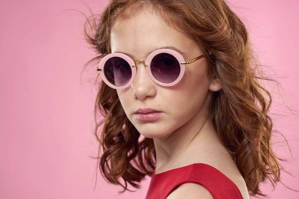 Dívka s kudrnaté vlasy tmavé kulaté brýle zábava červené šaty růžové pozadí — Stock fotografie