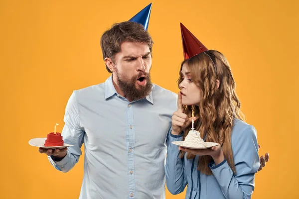 Uomo e donna a una festa in berretti e con fili di lame torta divertente sfondo giallo — Foto Stock