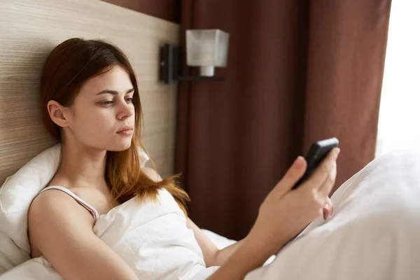 一个女人躺在床上用白色毯子和手机的肖像 — 图库照片