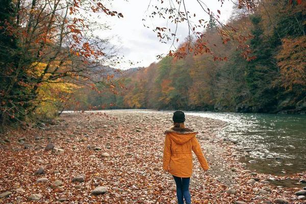 一个穿着黄色夹克的女人在河边的山里 — 图库照片