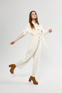 Hafif arka planda şık bir tulum ve çizme giymiş bir kadın.