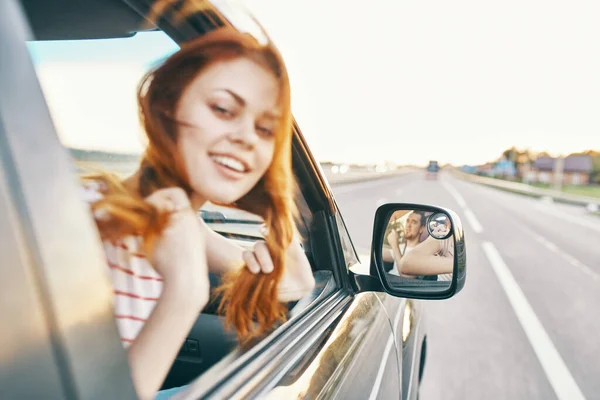 Ευτυχισμένη κοκκινομάλλα γυναίκα κοιτάζει έξω από το παράθυρο του αυτοκινήτου και οδηγεί στο δρόμο, κομμάτι καλοκαιρινές διακοπές — Φωτογραφία Αρχείου