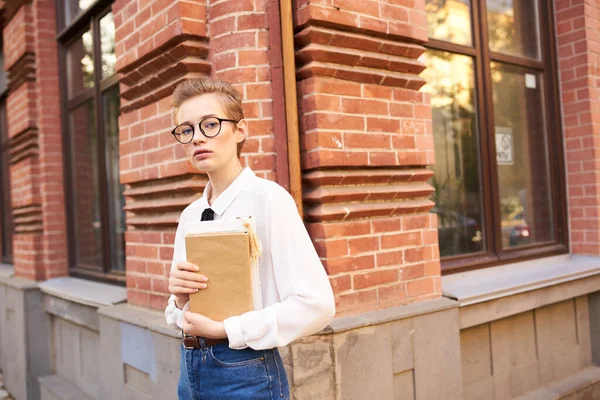 Krásná žena s krátkými vlasy drží zápisník v ruce a stojí v blízkosti cihlové budovy na ulici — Stock fotografie