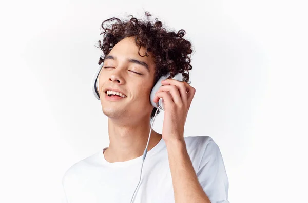 Emotionell man med lockigt hår och i hörlurar lyssnar på musik ljus bakgrund — Stockfoto