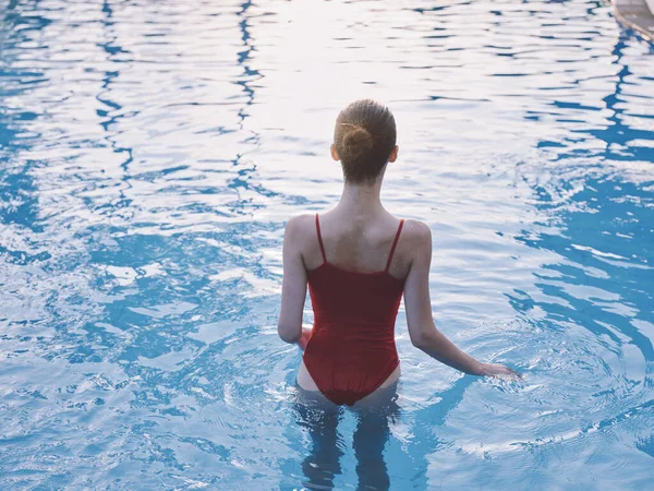 Mulher romântica em maiô vermelho caminha para a água transparente da piscina vista traseira — Fotografia de Stock