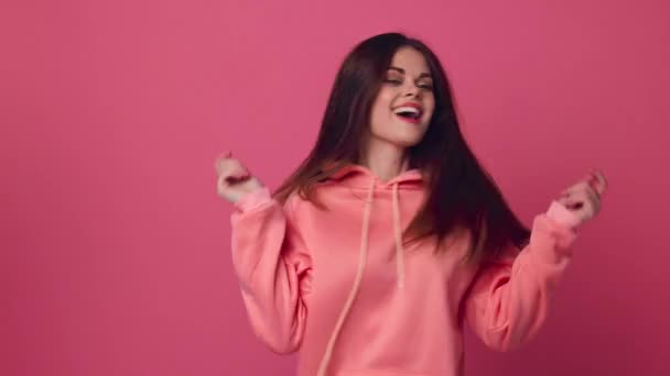 Молода жінка танцює і красиво позує на рожевому тлі в рожевому светрі — стокове відео