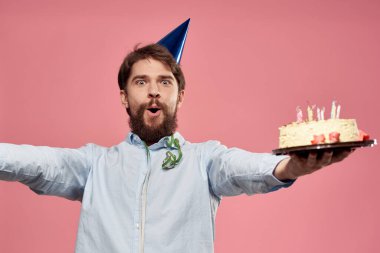 Pastalı ve mavi gömlekli bir adam pembe arka planda doğum günü tatili manzaralı.