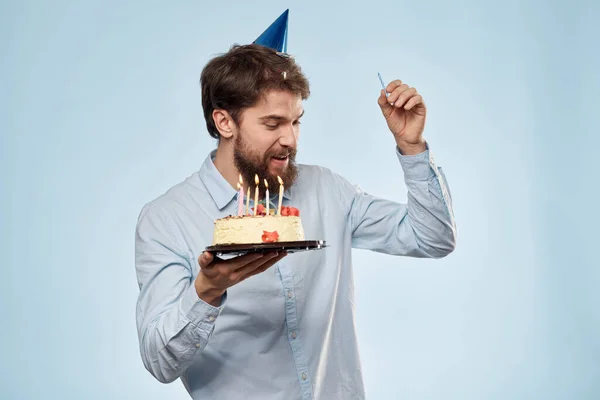 Hombre con un plato de pastel y una vela festiva fondo azul gorra fiesta corporativa — Foto de Stock