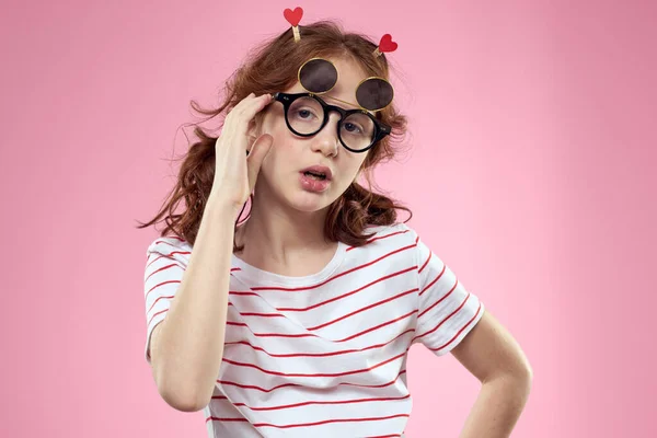 유행하는 안경을 쓰고 머리 뒤에서 핑크 색 배경의 마음을 품고 있는 소녀 — 스톡 사진