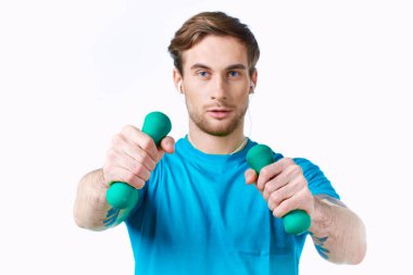 Elinde dambıllar olan mavi tişört egzersiz kulaklıkları olan bir adam.