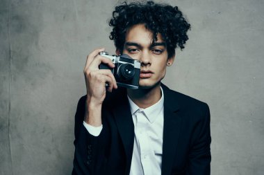 Gri arka planda kameralı fotoğrafçı ve ceket kıvırcık gömlek modeli.