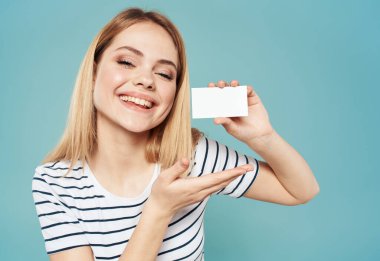 Mavi arka planda mutlu bir kadın elleri ve elinde bir kartvizitle el kol hareketi yapar.