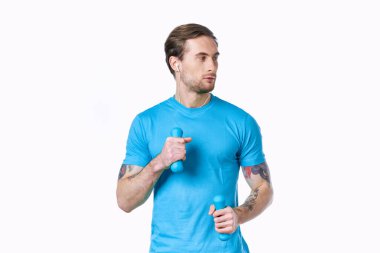 Hafif arka planda mavi tişörtlü, dambılı adam yana bakıyor.