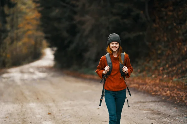 Donna con uno zaino in piena crescita cammina lungo la strada nel bosco in autunno — Foto Stock