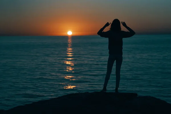 Silhueta de uma mulher ao pôr do sol perto do mar gesto com as mãos para trás vista — Fotografia de Stock