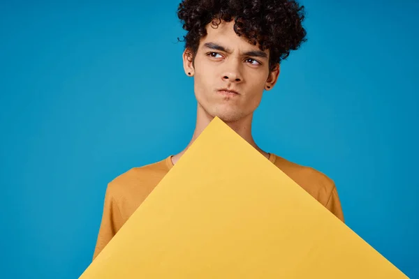 Cheerful guy with curly hair of yellow asters in his hands studio blue background Stock Image