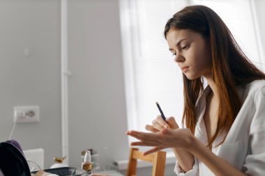 Bir kadın elinde kalem, masaya oturmuş göz kalemi kullanıyor.