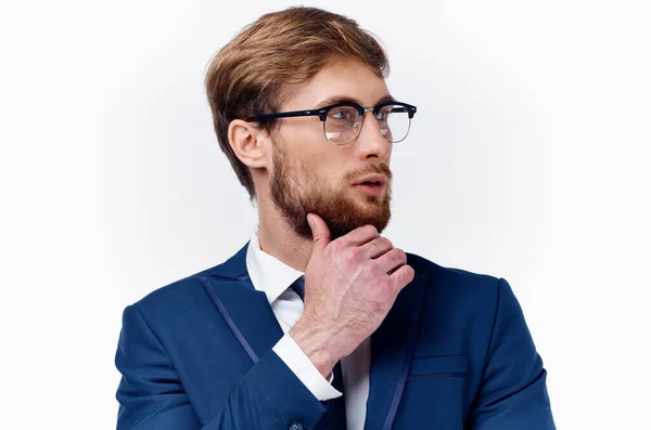 Homme d'affaires en costume et lunettes tient sa main près de son visage sur un fond clair veste bleue cravate classique — Photo