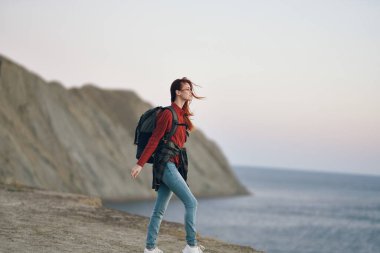 Sahilde deniz kenarındaki dağlarda sırtında sırt çantası olan bir kadın.