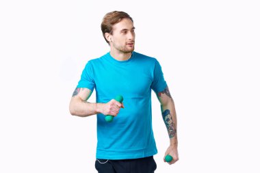 Elinde dambıllar olan mavi tişörtlü bir sporcu spor salonu dövmesi yaptırıyor.