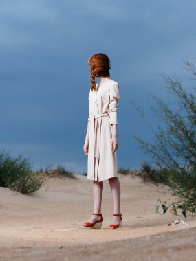 Uzun boylu, kızıl saçlı, yüzünde atkuyruğu olan, kırmızı ayakkabılı bir kadın.