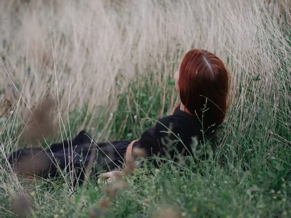 Nő fekete ruha a füvön az erdőben vörös haj modell oldalnézet — Stock Fotó