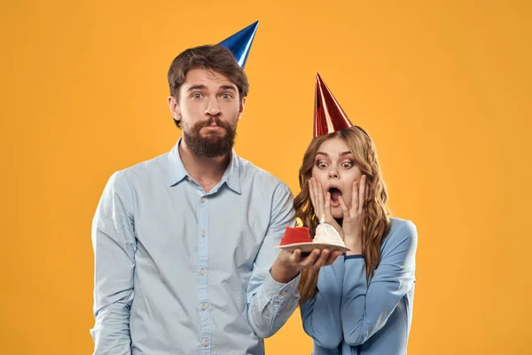 Feliz homem e mulher com bolo de aniversário no fundo amarelo — Fotografia de Stock