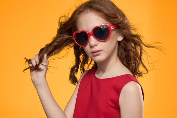 하트를 쓰고 선글라스를 쓴 빨간 드레스를 입은 소녀가 노란 배경의 젊은 시절 스튜디오에서 — 스톡 사진