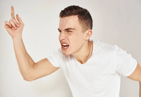 Homme émotionnel dans un T-shirt blanc gestes avec ses mains sur un fond léger modèle stress irritabilité — Photo