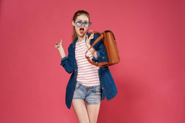 Gözlüklü, şık elbiseli güzel bir kadın sırt çantası, pembe arka plan modeli.