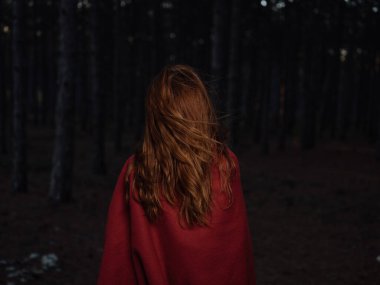 Omuzlarında kırmızı bir ekoseyle geceleri ormanda dolaşan bir kadın.