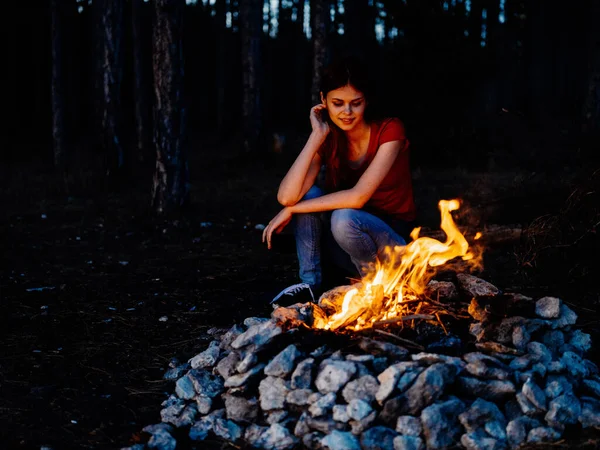 Μια γυναίκα κάθεται κοντά στη φωτιά και κοιτάζει τη φωτιά σε ένα πευκοδάσος — Φωτογραφία Αρχείου